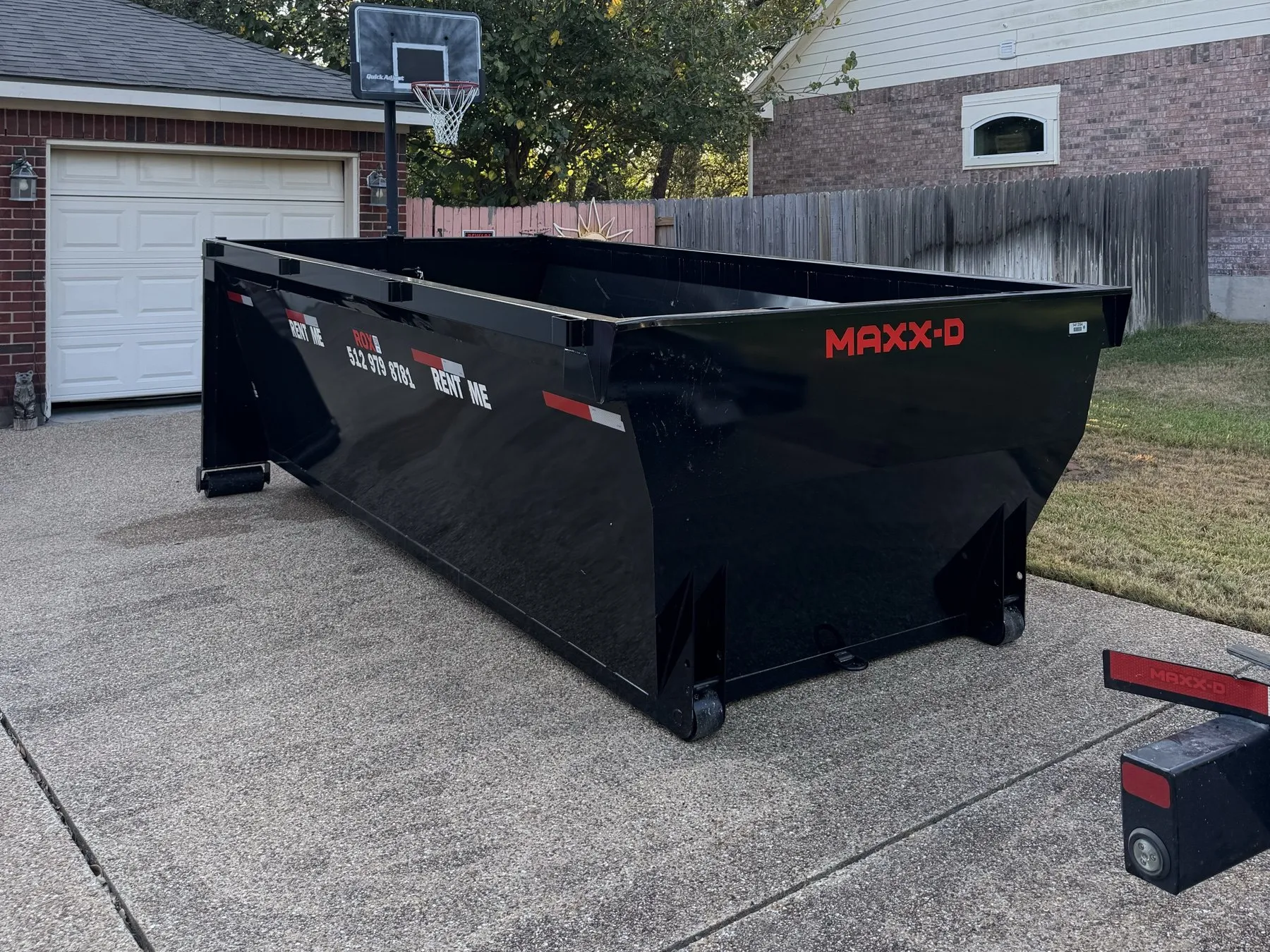 Empty roll-off dumpster set on a driveway beside a garage
