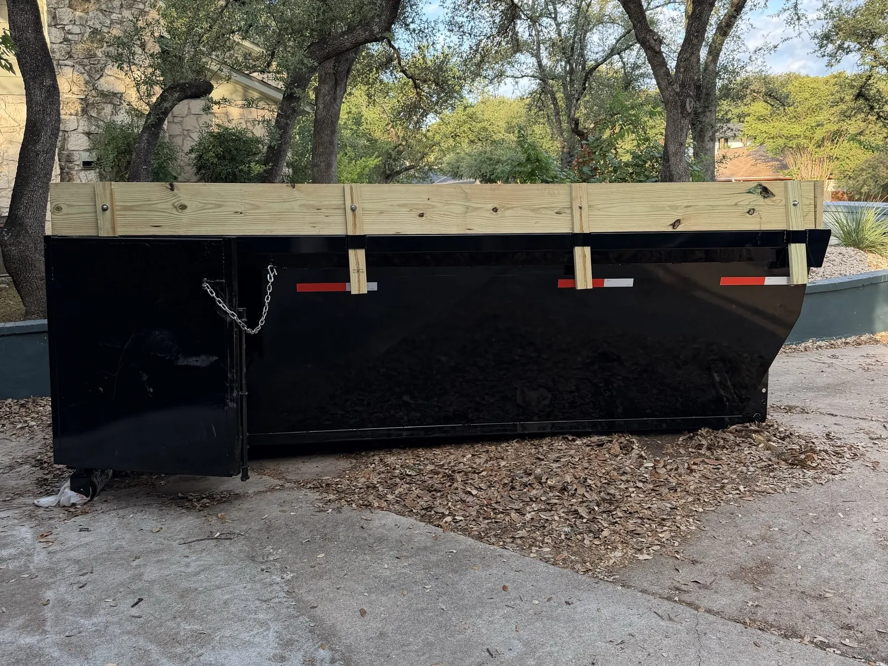 Dumpster with raised side boards under oak trees at a remodel