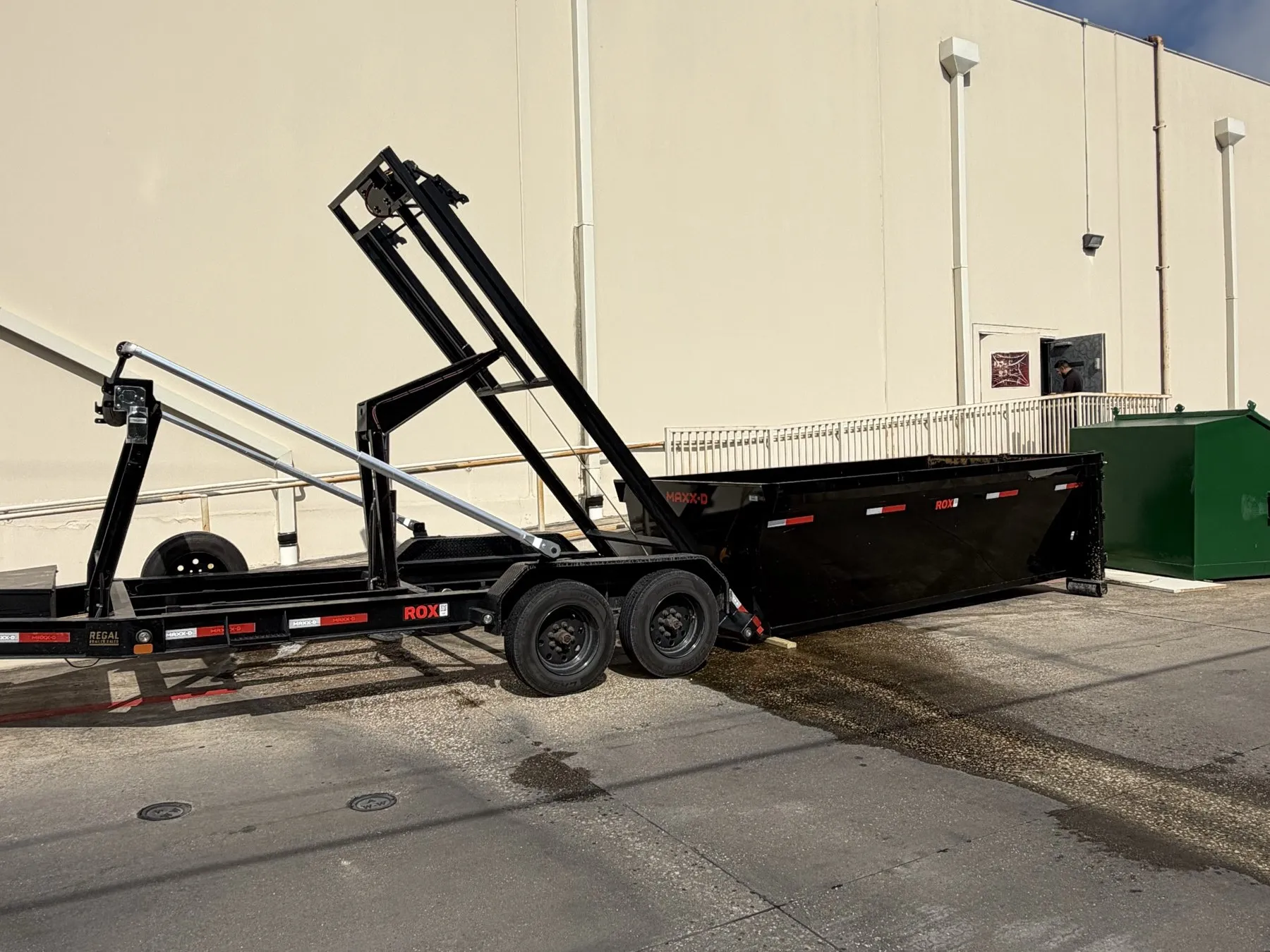Roll-off trailer setting a dumpster down behind a commercial building