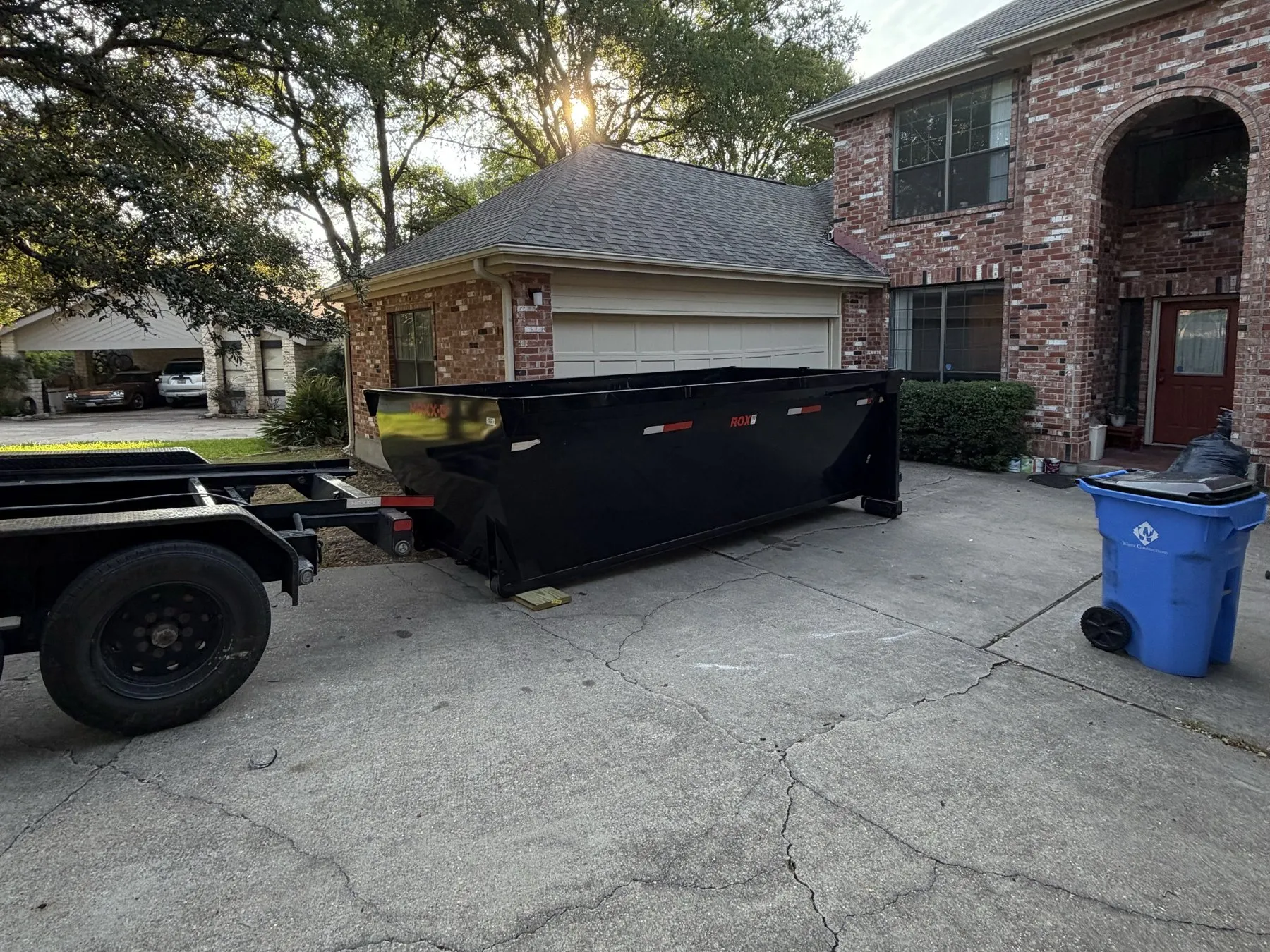Dumpster being delivered to a brick home at sunset