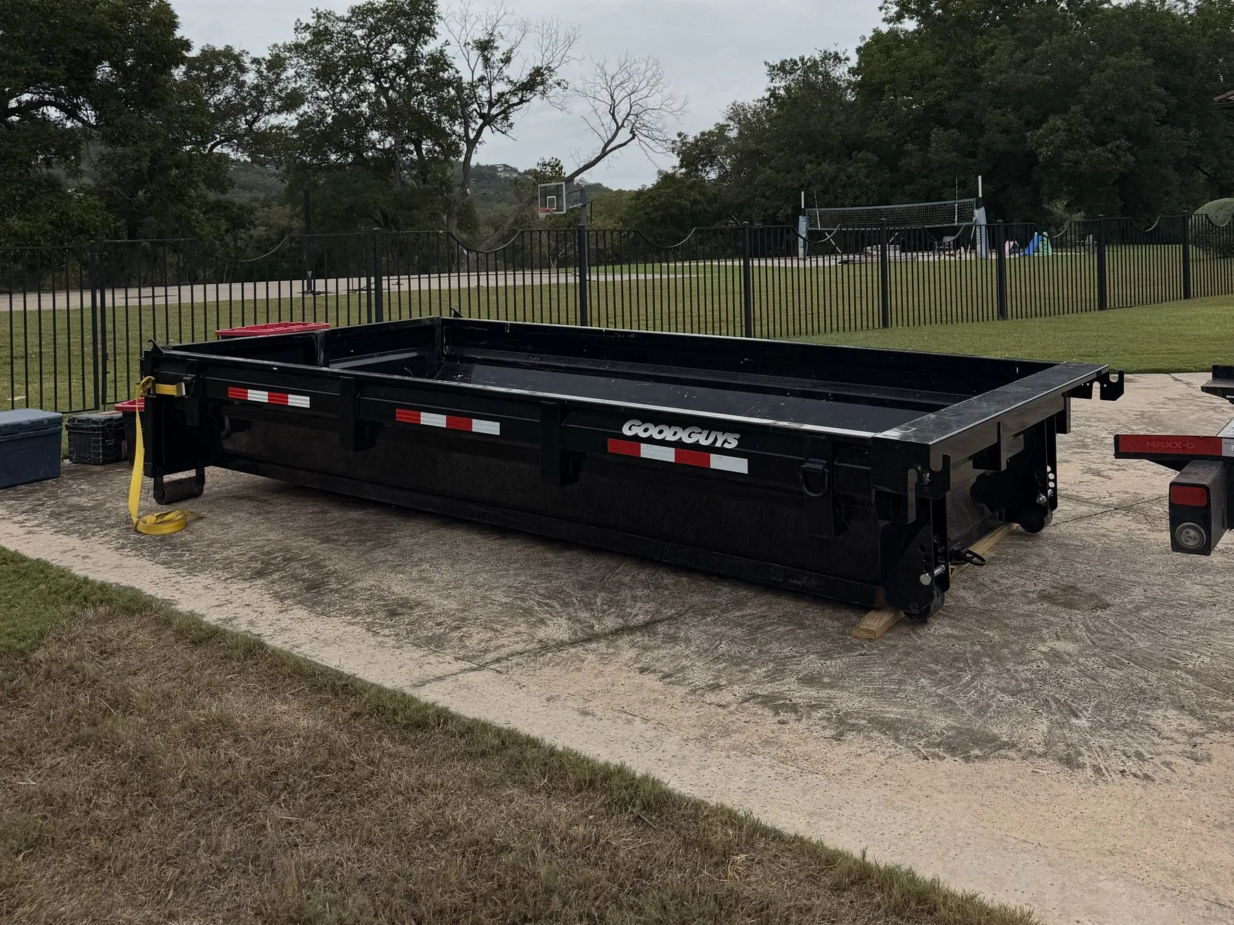Low-sided dumpster on a concrete pad beside a fenced field